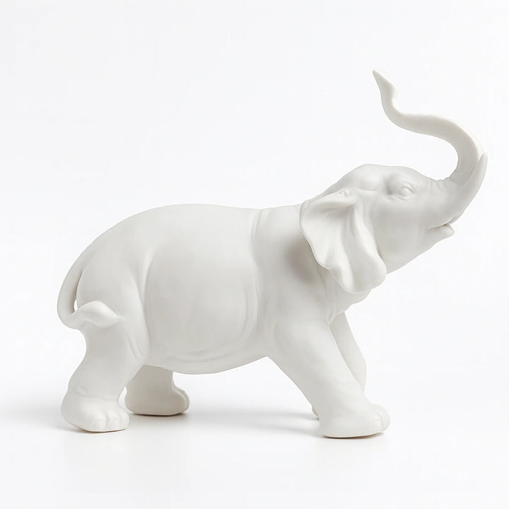 White ceramic elephant figurine in right-facing profile with its trunk raised on a white background