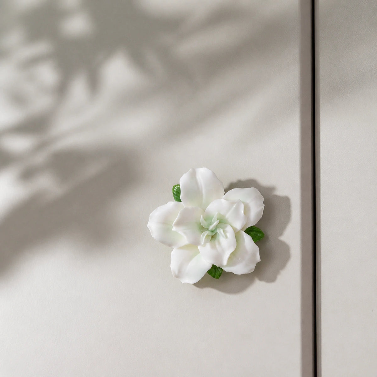 Pale green ceramic lily magnet styled with soft botanical light on a mushroom-gray cabinet.