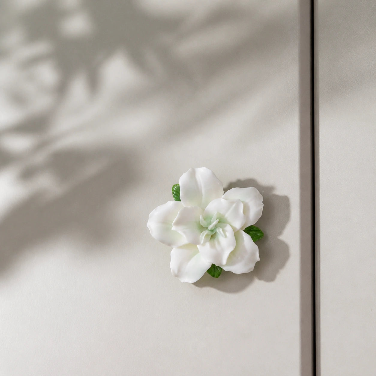 Pale green ceramic lily magnet styled with soft botanical light on a mushroom-gray cabinet.