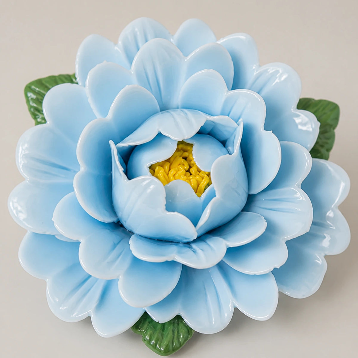 Gros plan des pétales émaillés bleu poudré, du cœur jaune et des pointes de feuilles vertes.