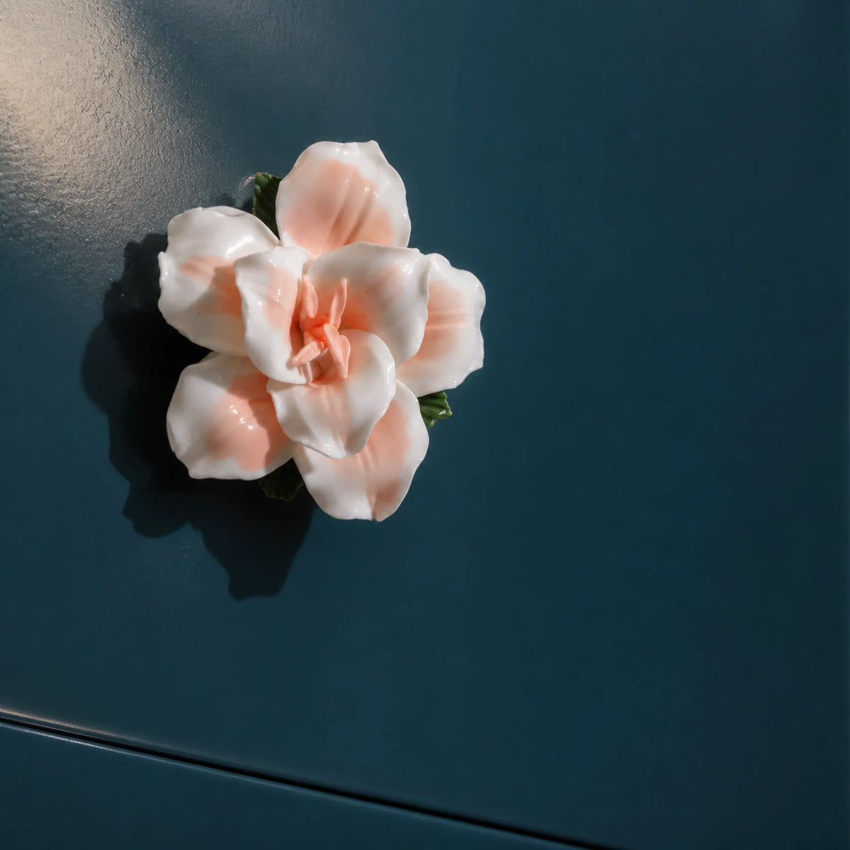 Soft orange ceramic lily magnet styled as a warm accent on a dark petrol magnetic surface.