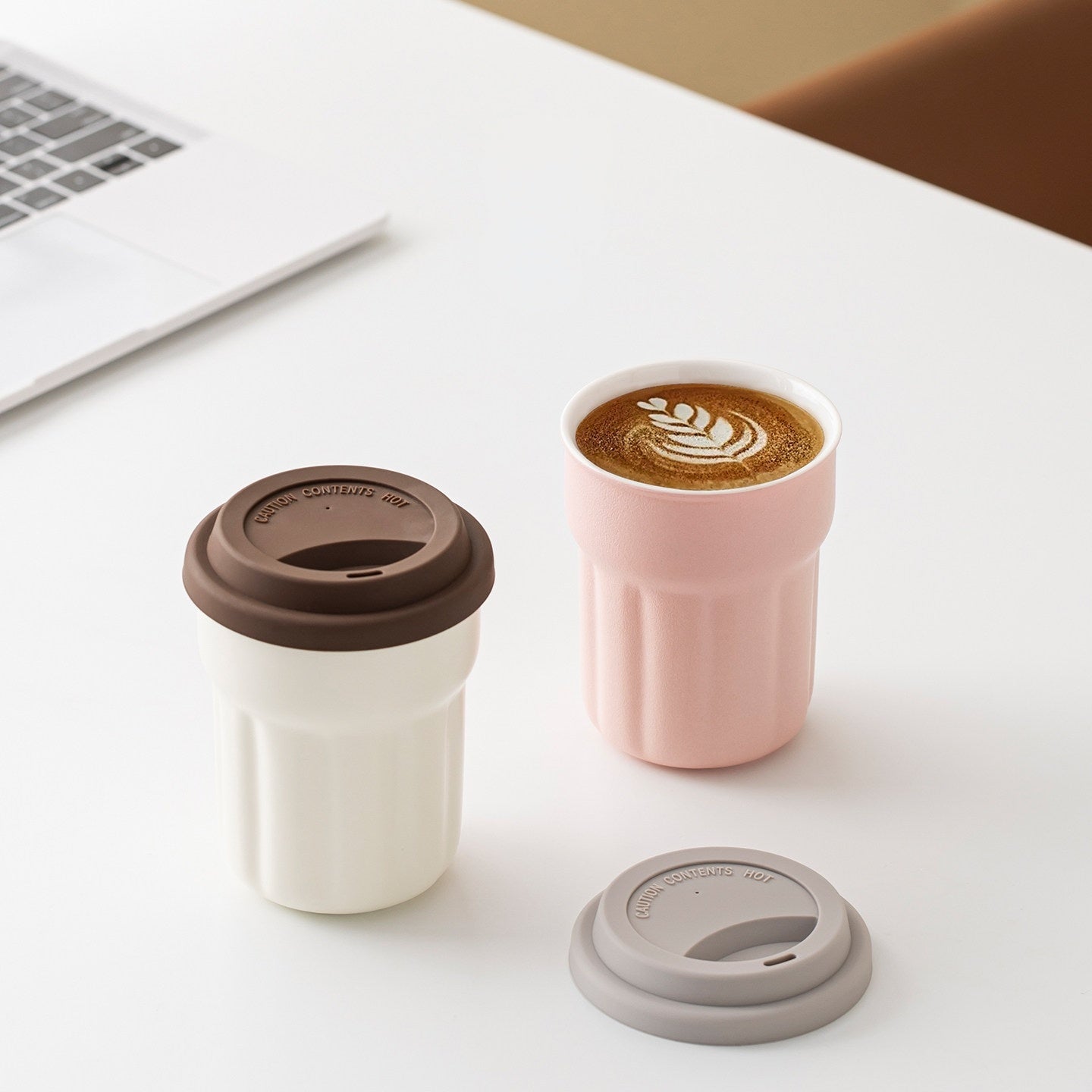 Blush pink and cream fluted ceramic mugs with removable silicone lids on a desk
