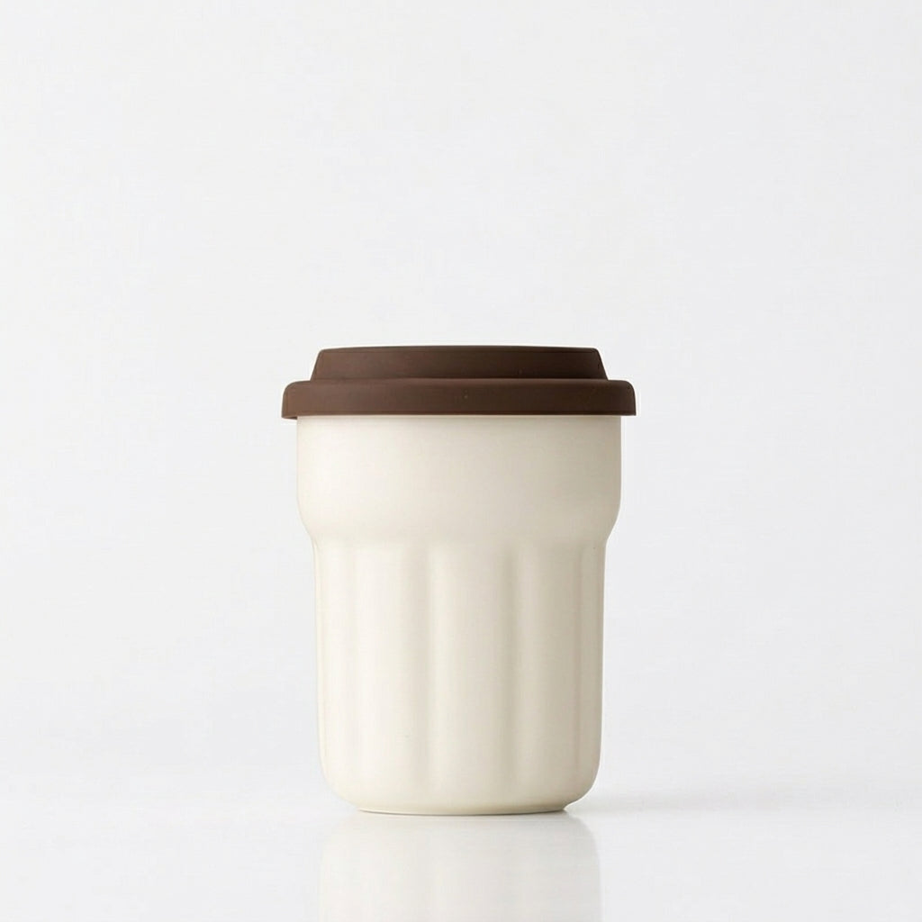 Cream fluted ceramic travel mug with brown sliding lid on a white background