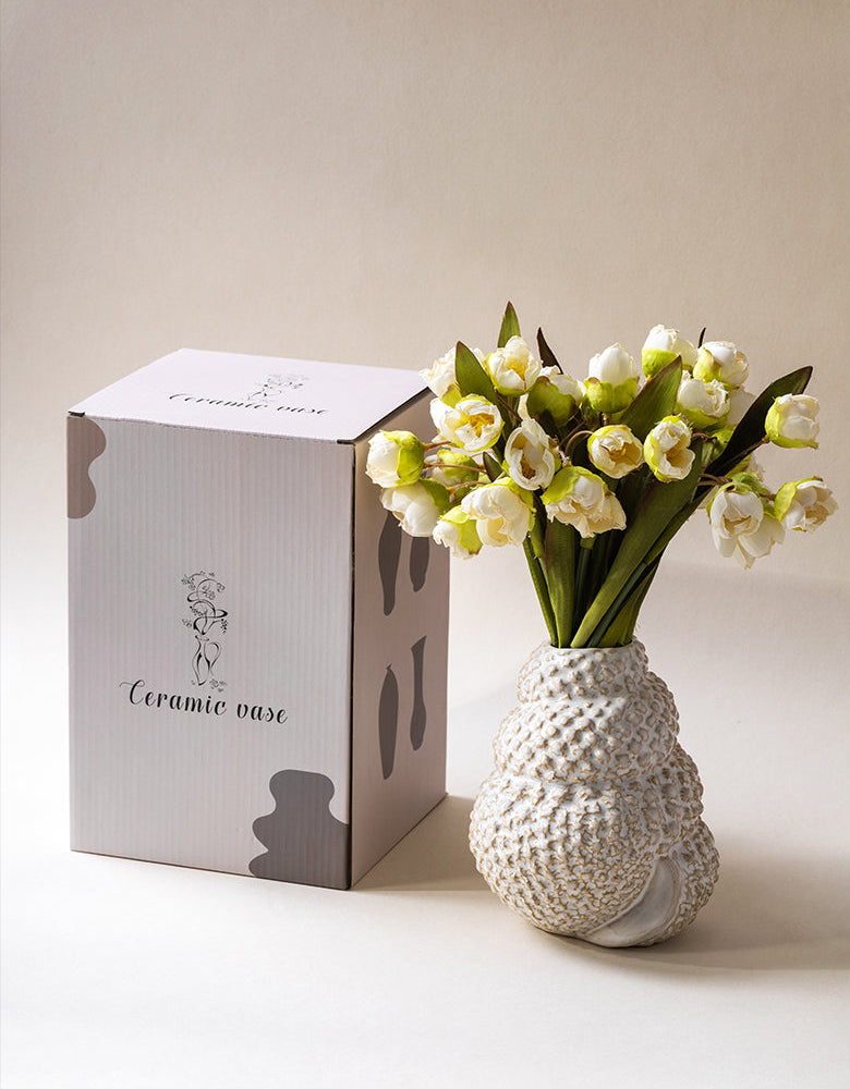 Ceramic vase with flowers next to its packaging on a light background