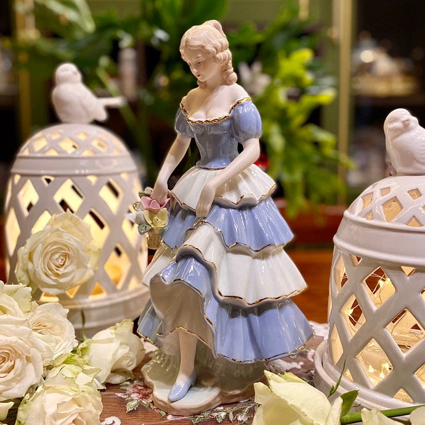 Decorative figurine of a woman in a blue dress with two lanterns and flowers on a table.