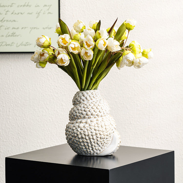 White textured vase with flowers on a black surface against a light wall.