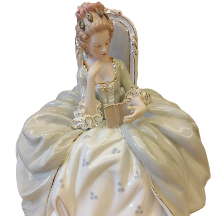 Front view of a seated porcelain reading lady in a pale green gown with a brown book and flowered hair