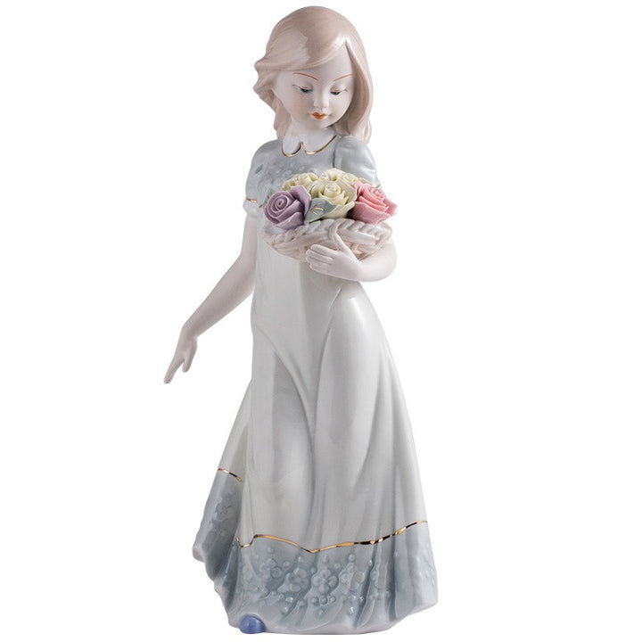 Standing girl figurine in a pale gray-and-white dress with gold trim, holding a rose basket on a white background.