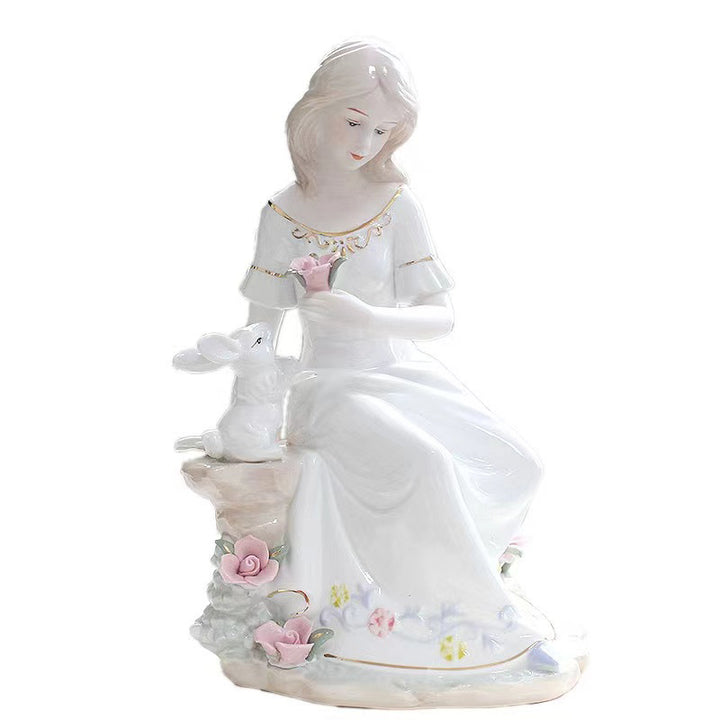 Porcelain figurine of a seated woman holding a pink rose beside a white rabbit on a flower-accented base.