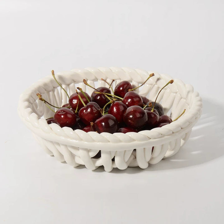 Round white lattice ceramic basket filled with dark red cherries on a white studio background.