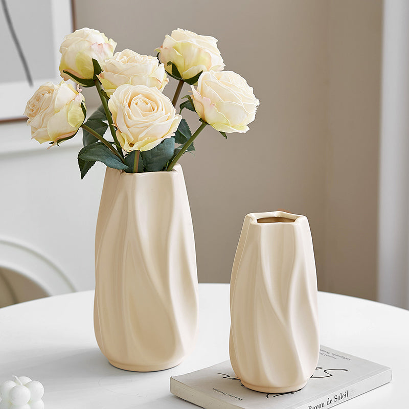 Cream-colored ceramic vases with textured wavy design on white table, one holding pale yellow roses