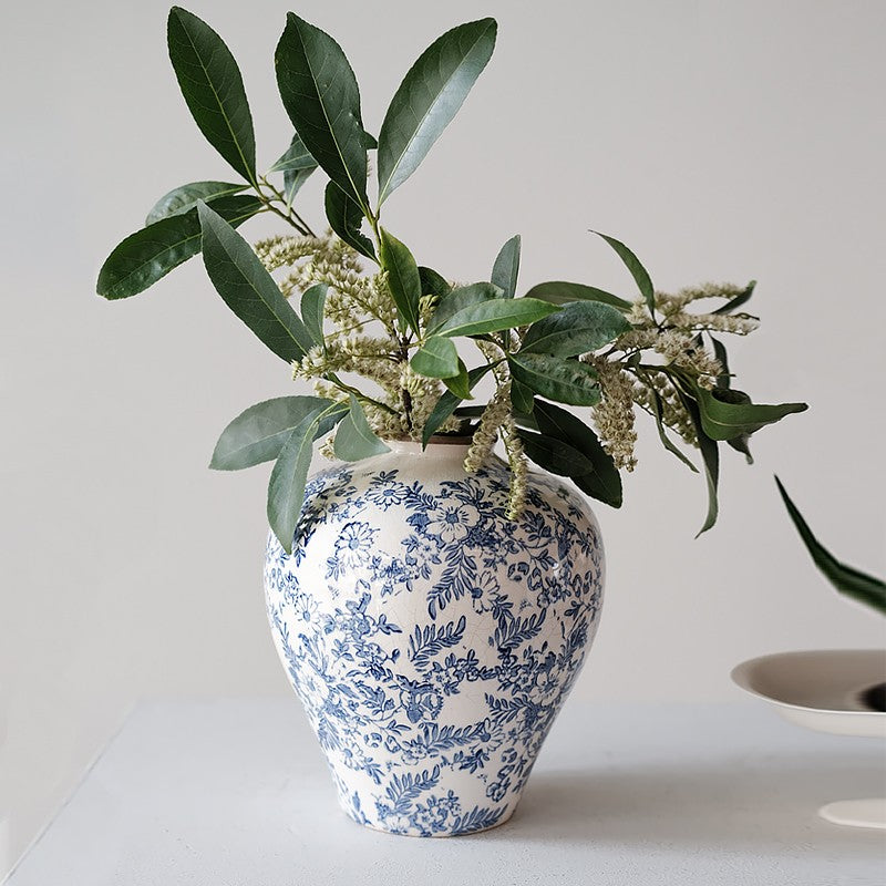 Blue and white patterned vase with green leaves on a light background