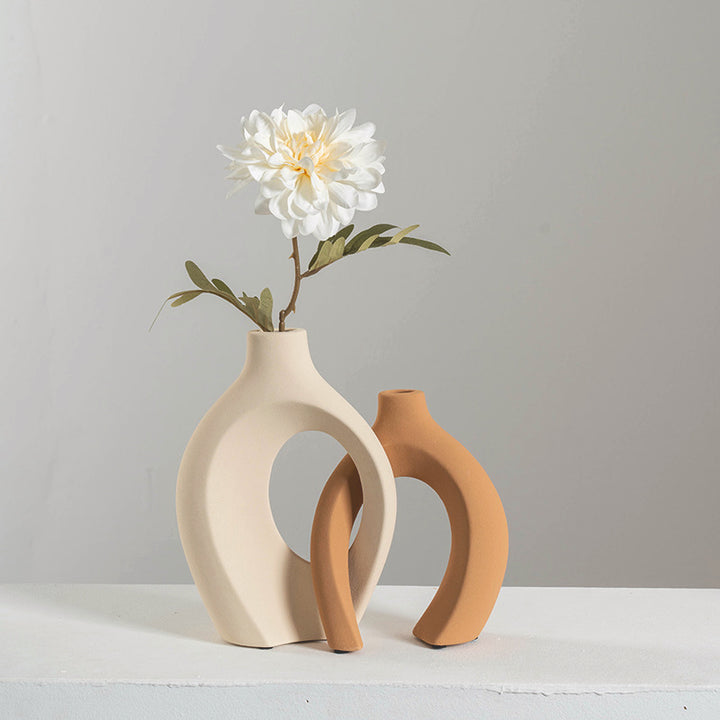 Modern beige and terracotta ceramic vases with round cutouts and a white flower on gray background