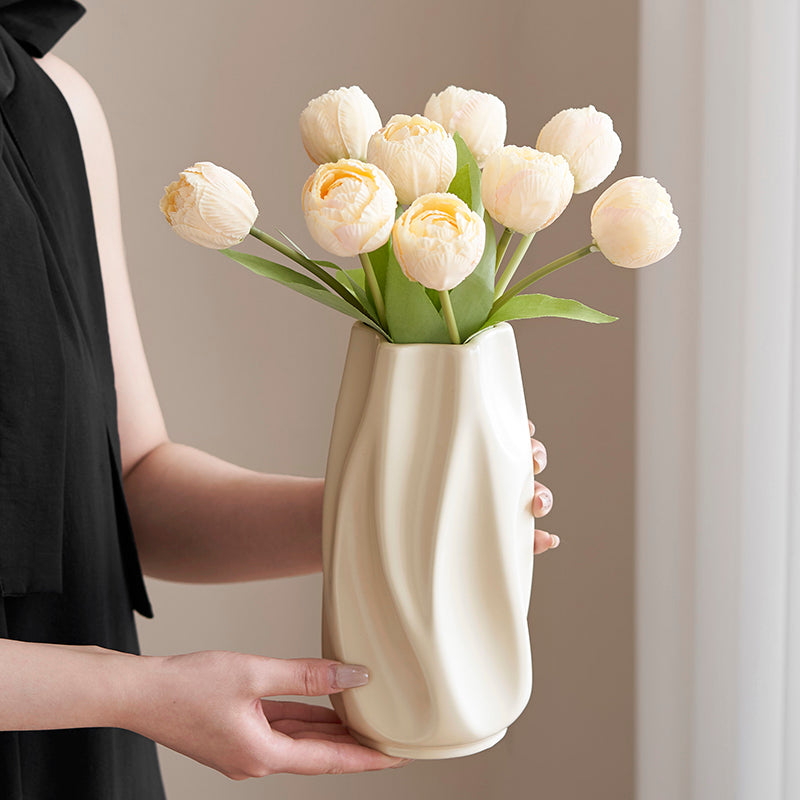 Hands holding modern cream ceramic vase with artificial pale yellow tulips against neutral background