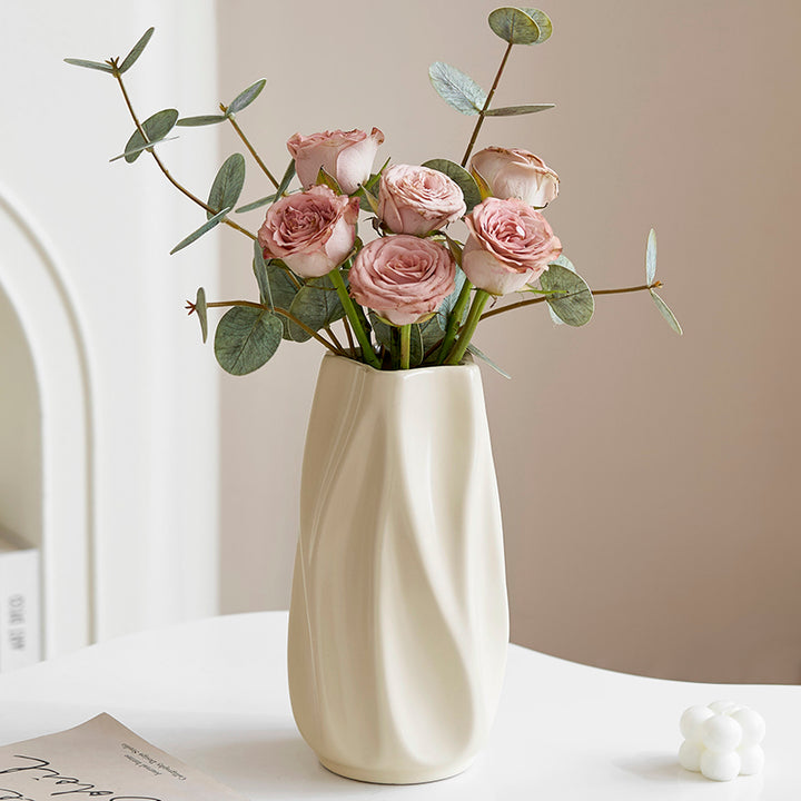 Elegant beige ceramic vase with pink roses and eucalyptus branches on white table
