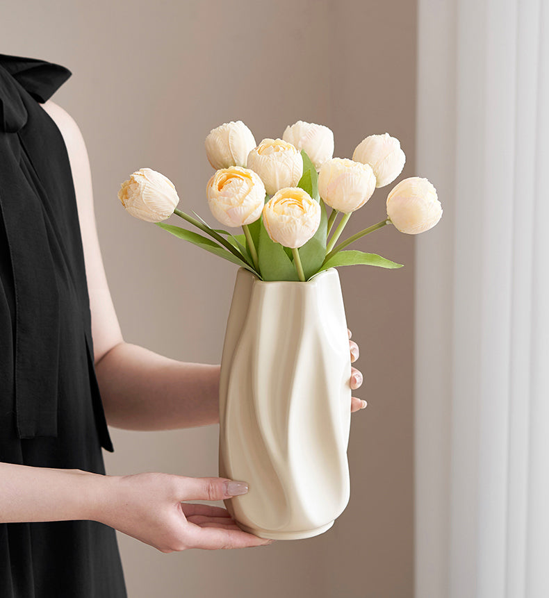 Woman in black dress holding modern cream ceramic vase with light peach tulip flowers