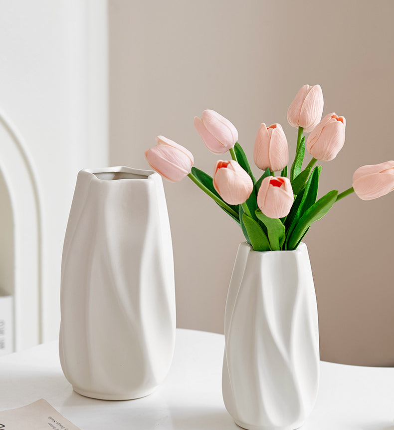 Elegant white ceramic vases with twisted design, one holding soft pink tulips on white table