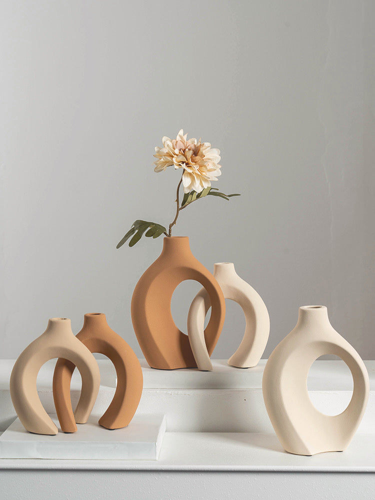 Modern abstract terracotta and beige ceramic vases with a single cream flower on white surface