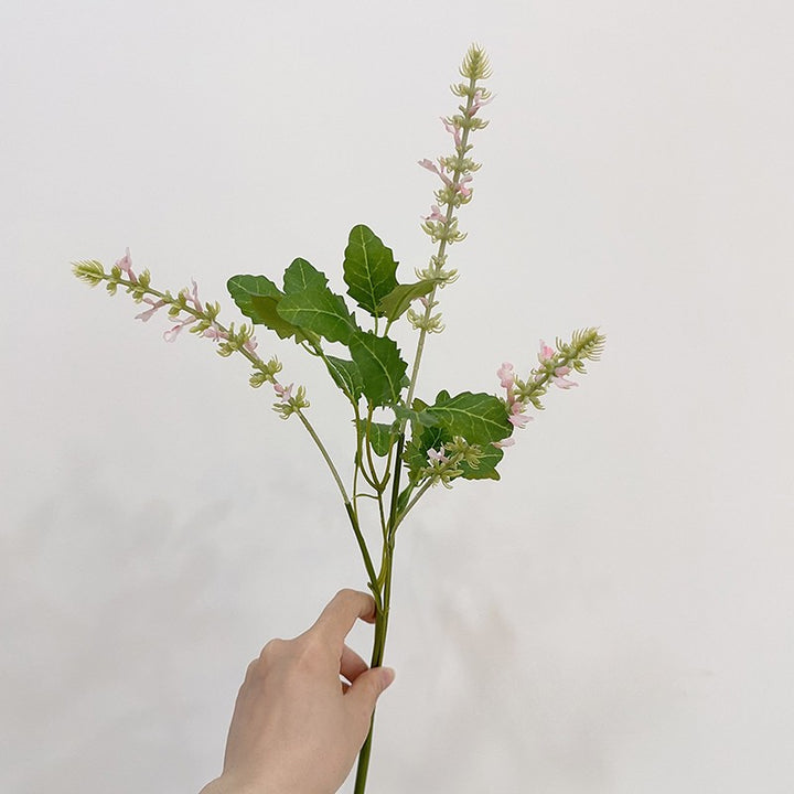 Faux meadow sage stems with pale pink blossoms on three branching spikes, held in hand against a white background.