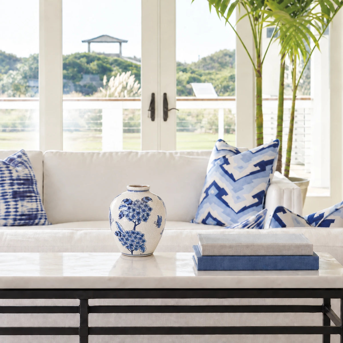 Small blue and white floral vase on a stone console beside blue and white sofa cushions.