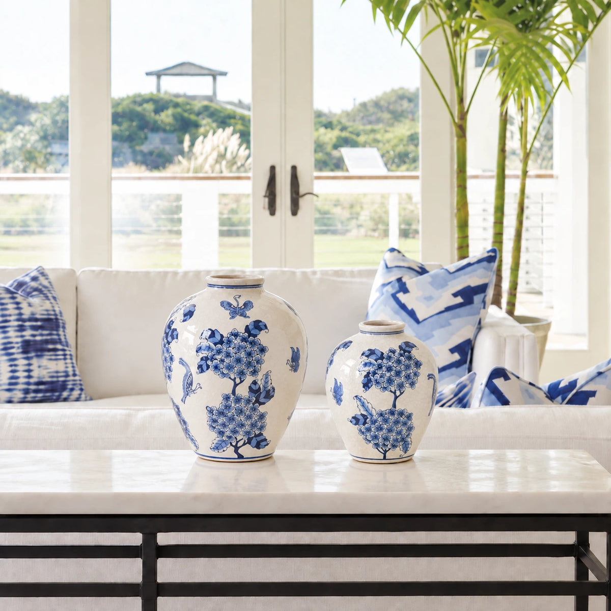 Small and large blue and white floral vases displayed together on a console in a bright living room.