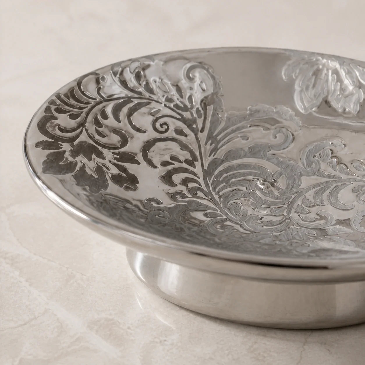 Close view of embossed floral scrollwork on a reflective silver ceramic soap dish