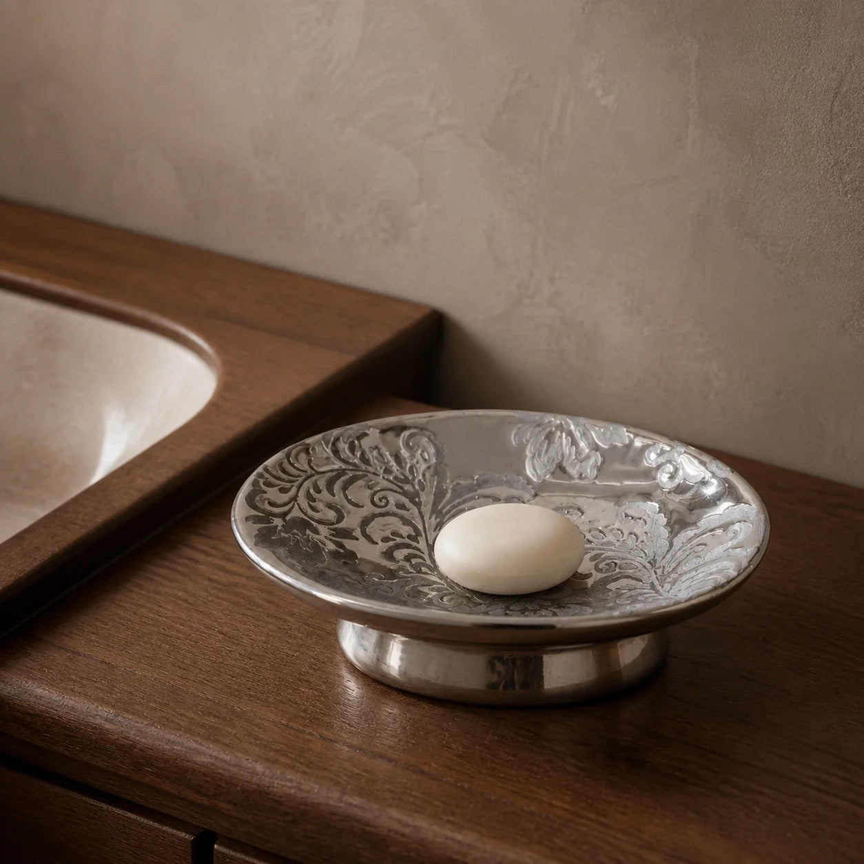 Silver-tone pedestal soap dish with an oval ivory soap on a dark wood bathroom vanity