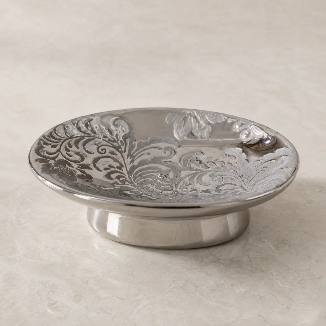 Baroque silver-tone ceramic soap dish with embossed floral relief on pale stone