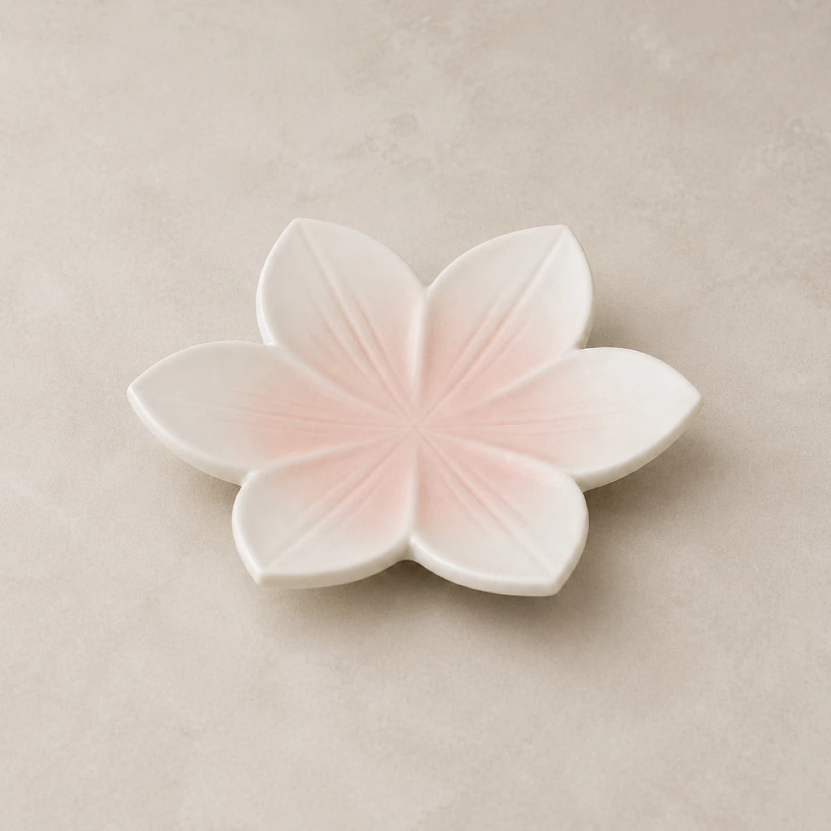Blushing Sakura ceramic soap dish with six blush-pink petals on a warm neutral background