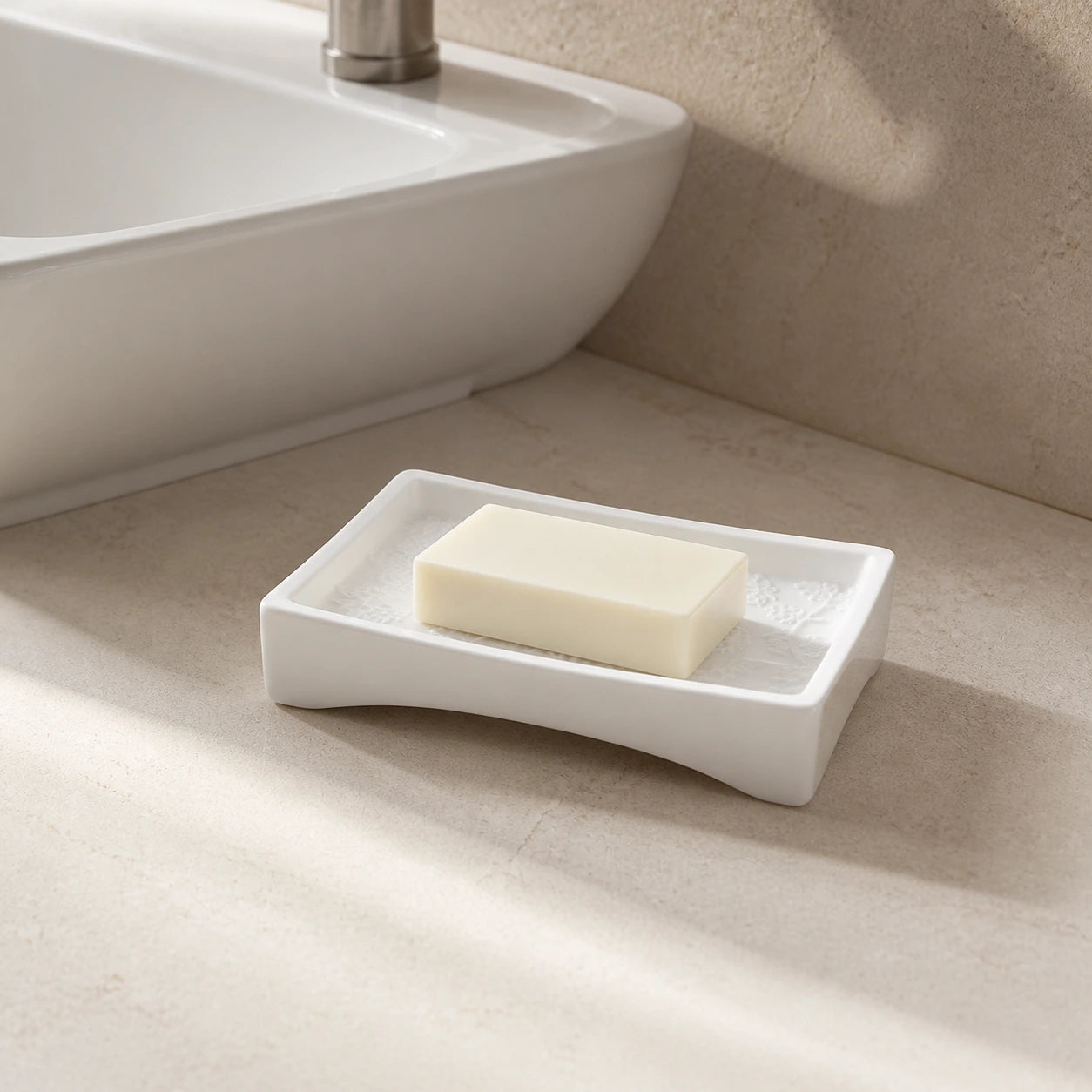 Weiße Keramik-Seifenschale mit botanischem Relief und elfenbeinfarbener Seife am Waschbecken