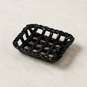 Empty Glossy Noir braided-rim ceramic soap basket on pale warm stone