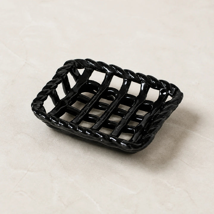 Empty Glossy Noir braided-rim ceramic soap basket on pale warm stone