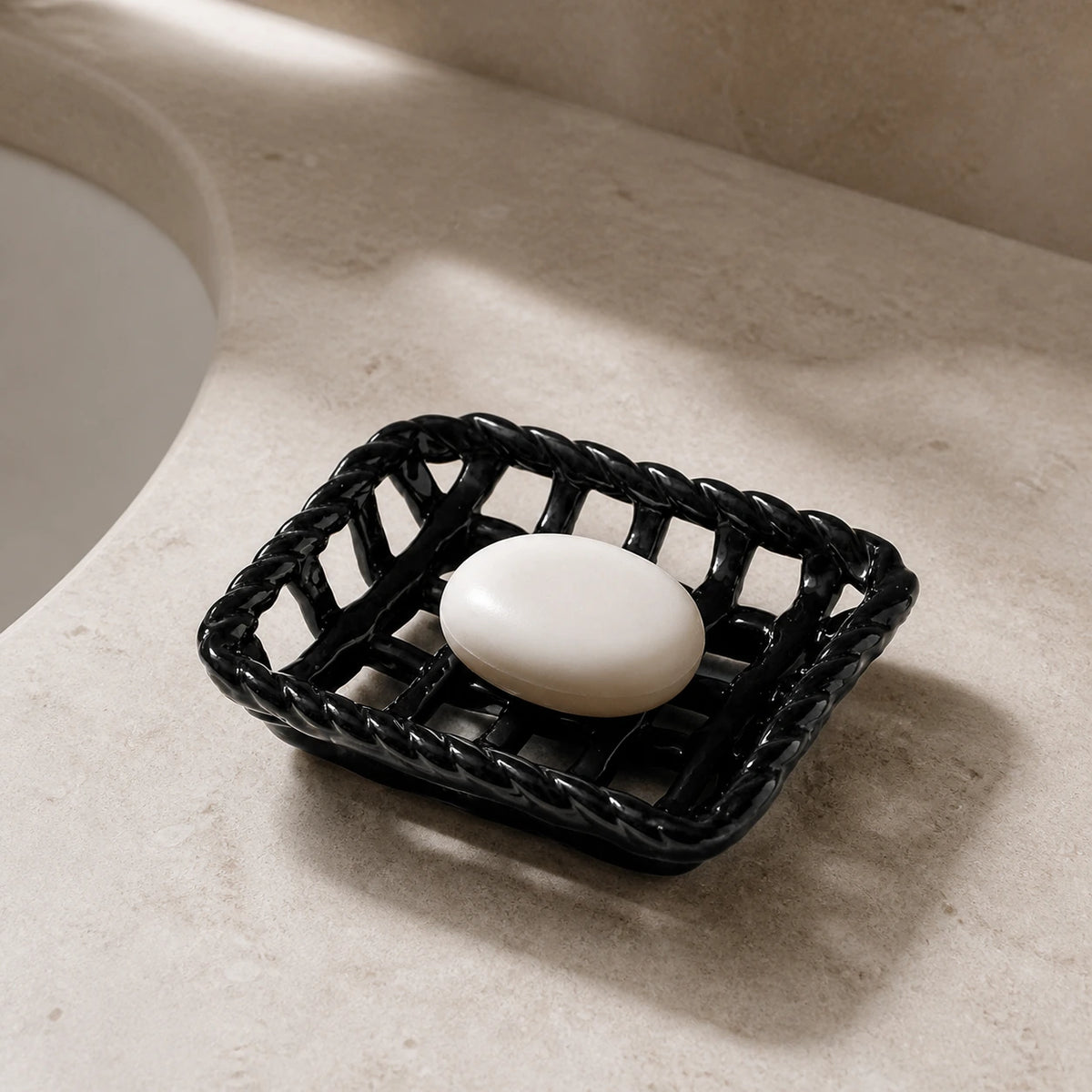 Glossy Noir ceramic basket holding oval guest soap on a warm stone counter