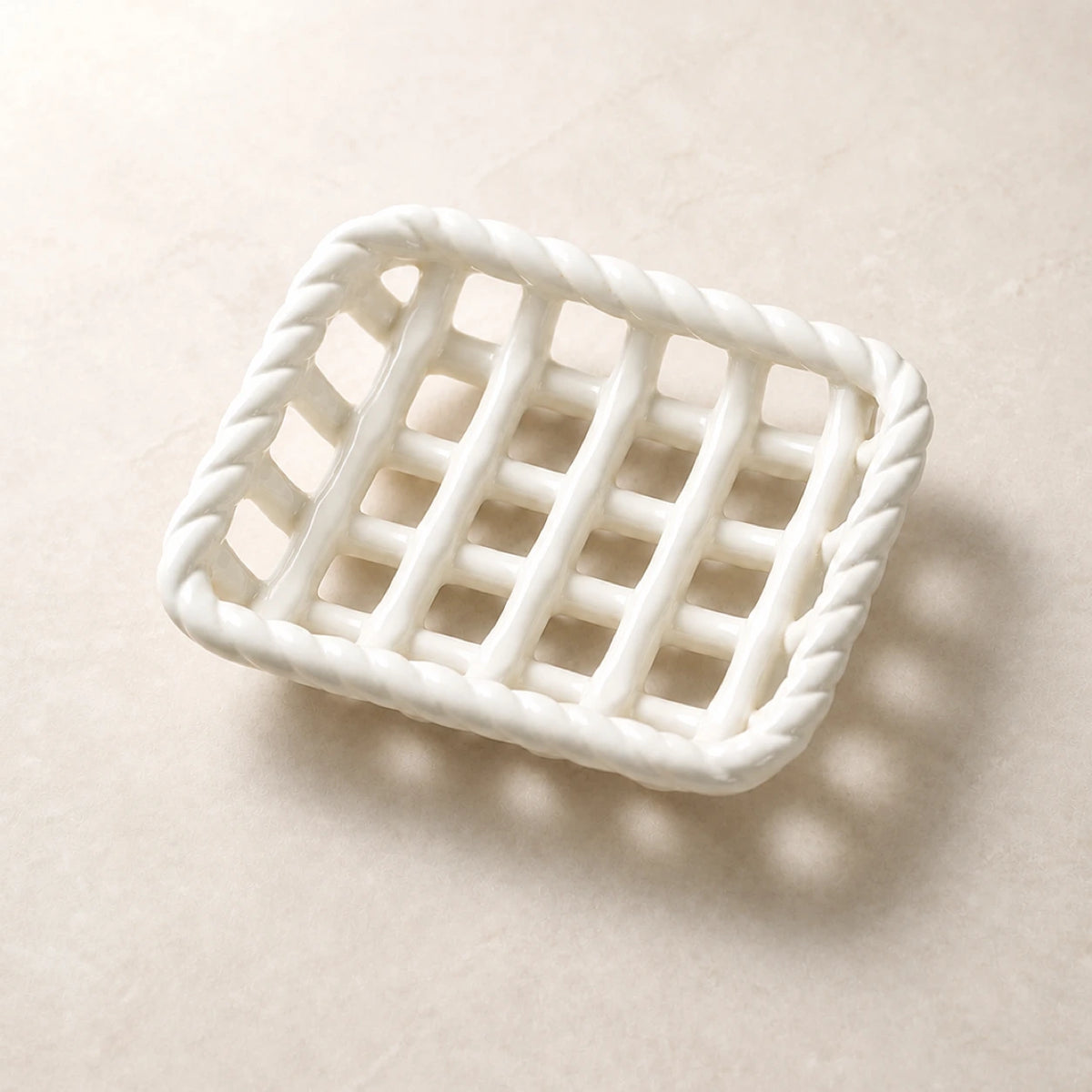 Empty Glossy White braided-rim ceramic soap basket on pale warm stone