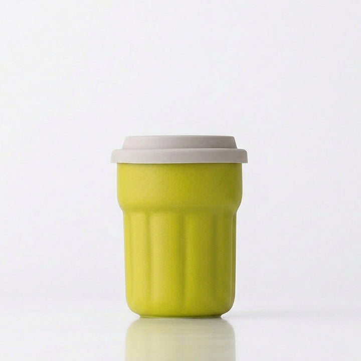 Lime green fluted ceramic travel mug with gray sliding lid on a white background