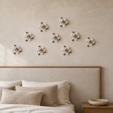 Multiple 7 cm Small Ruffled Peony ceramic wall flowers with plum purple accent arranged as a wall grouping in a warm neutral interior.