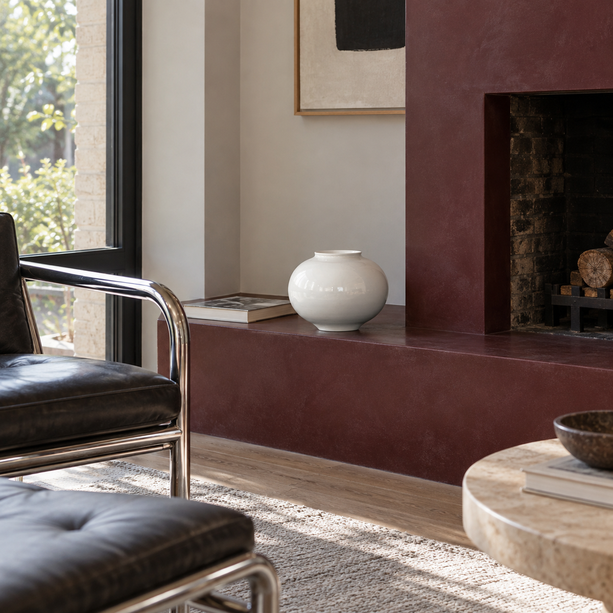 Small glossy white moon ceramic vase standing empty on a low burgundy fireplace ledge.
