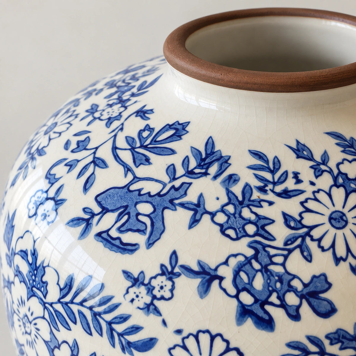 Close-up of the brown rim, ivory crackle glaze and cobalt floral pattern of a ceramic vase.