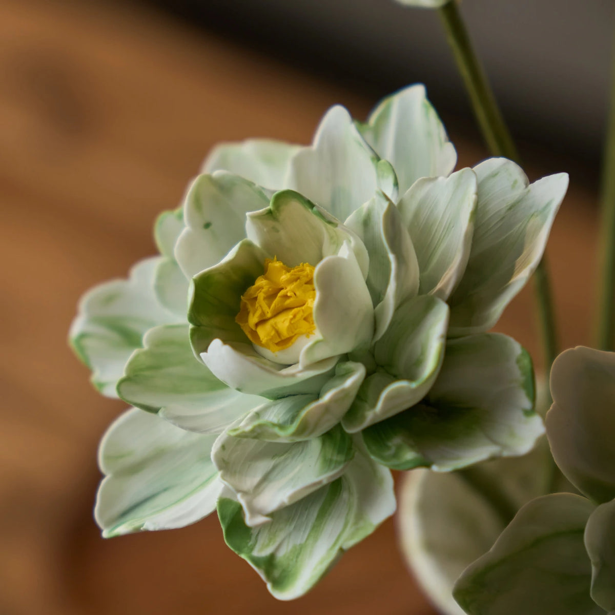 Close view of curled green-and-white marbled ceramic petals and a textured yellow flower centre.