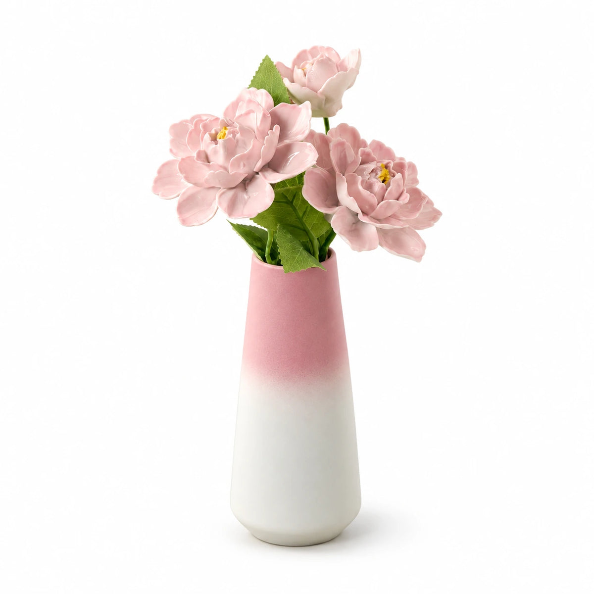 Three pink porcelain flowers in a pink-to-white tapered vase on a white background.