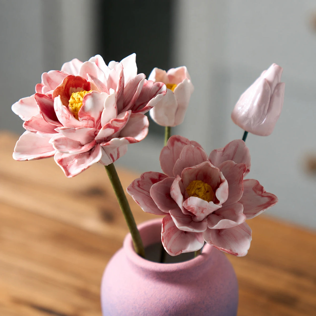 Close view of two pink marbled flowers, two smaller buds, thin stems and the textured pink vase opening.