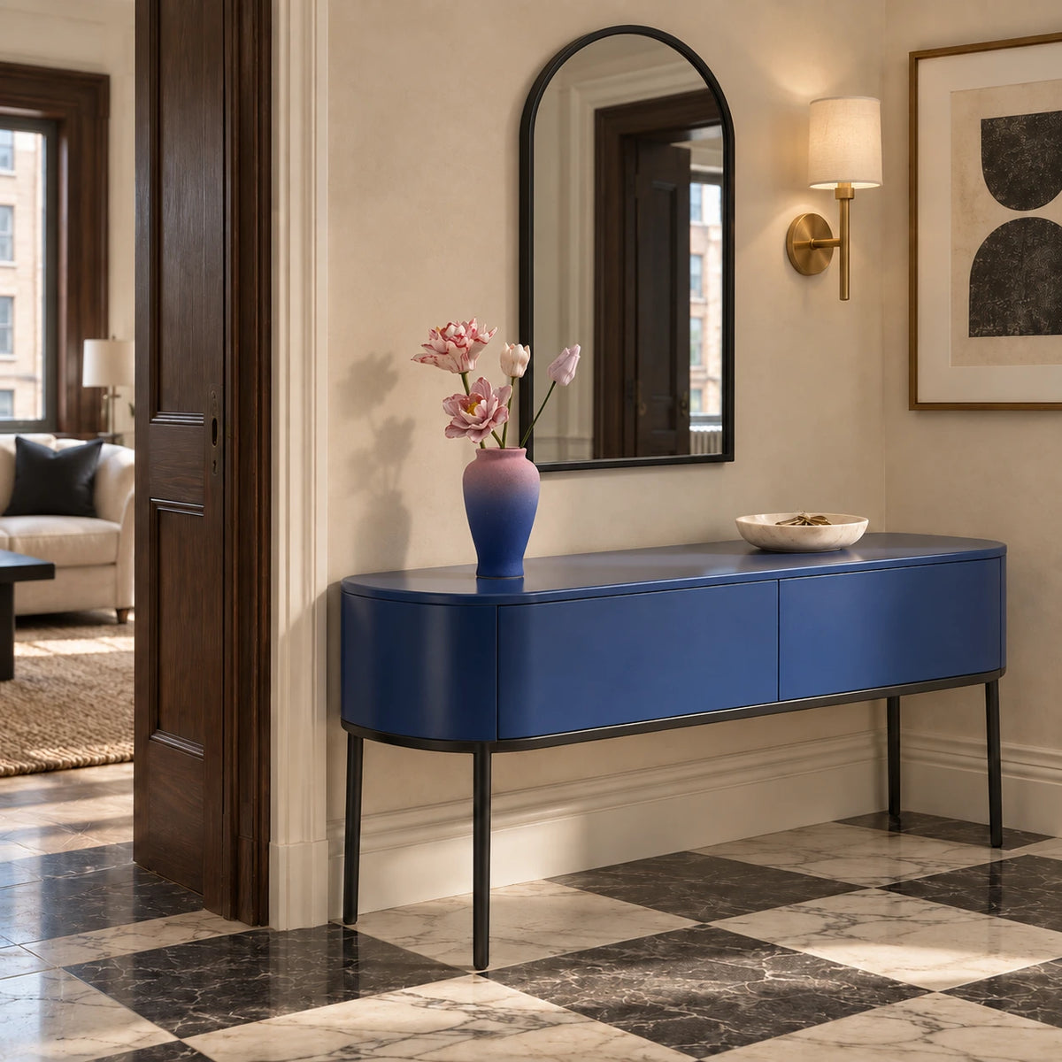 Two open pink flowers and two smaller buds in a textured pink-and-blue vase on a cobalt-blue entry console with an arched mirror and marble checker floor.