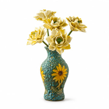 Five cream-yellow ceramic flowers in a textured turquoise vase with sunflower decoration on a white background.