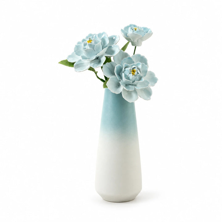 Three sky-blue porcelain flowers in a blue-to-white tapered vase on a white background.
