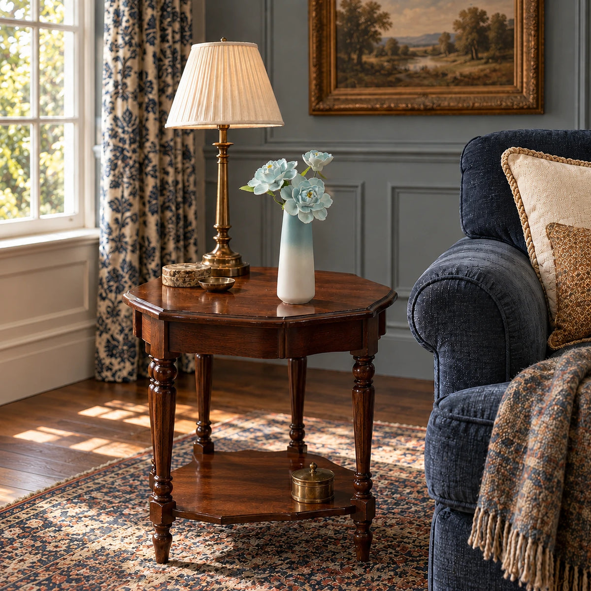 Three sky-blue porcelain flowers in a blue-to-white tapered vase on a mahogany side table beside a navy sofa, patterned curtains and a woven rug.