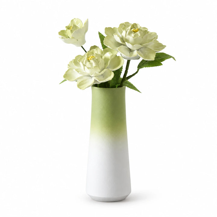 Three pale green porcelain flowers in a green-to-white tapered vase on a white background.