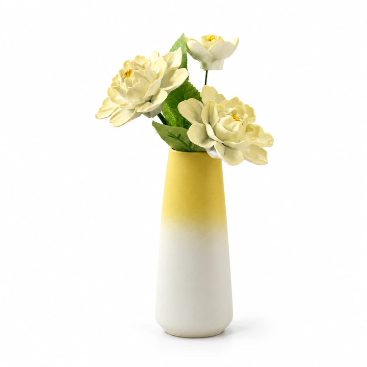 Three pale yellow porcelain flowers in a yellow-to-white tapered vase on a white background.