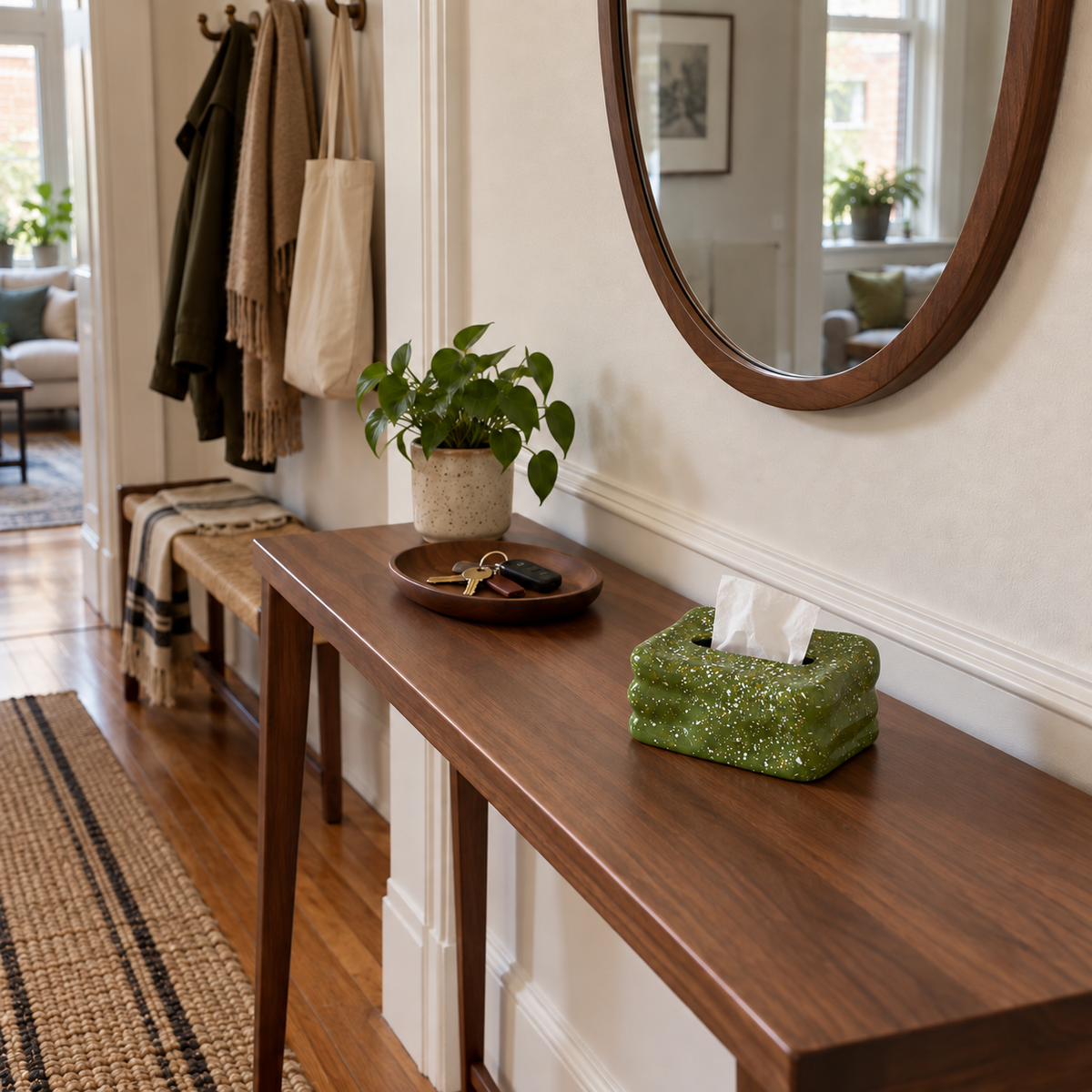 Olive-green speckled tissue box cover on a walnut hallway console beneath a wall mirror.