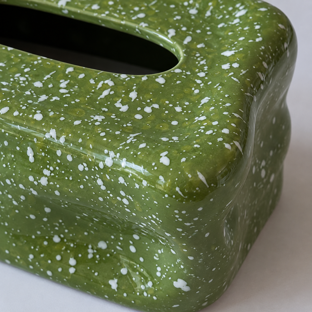 Close view of white flecks and glossy wavy folds on the olive-green ceramic tissue box cover.