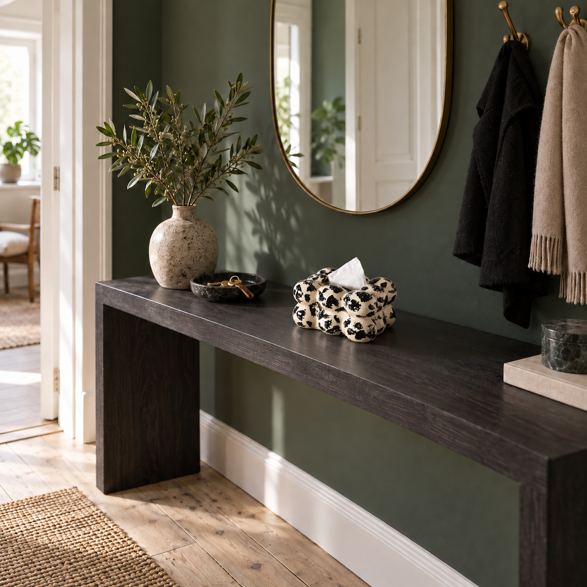 Black-and-ivory bubble ceramic tissue cover on a charcoal console in a green-walled entryway.